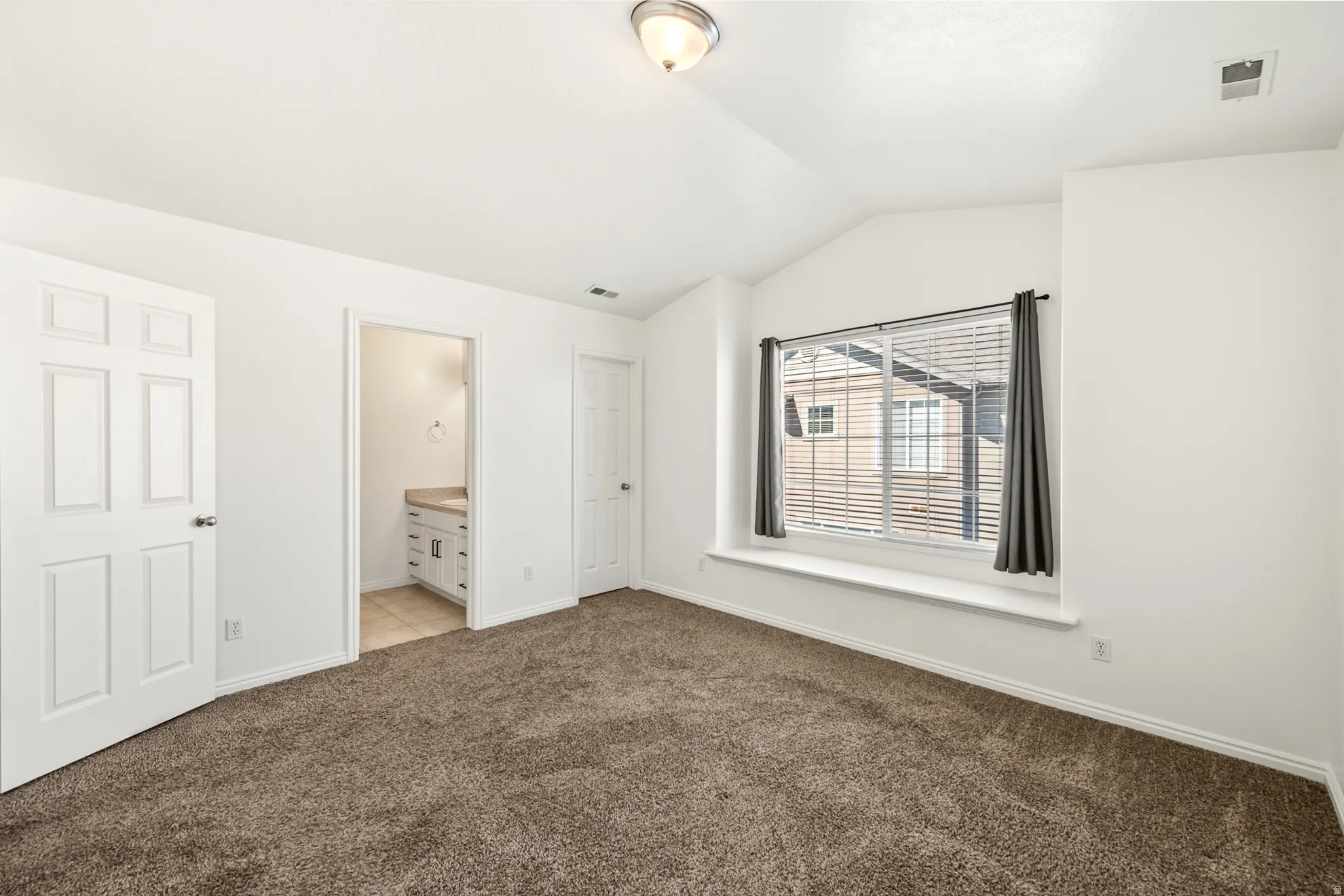 Carpeted room featuring a window with integrated seating, white trim, and a vaulted ceiling