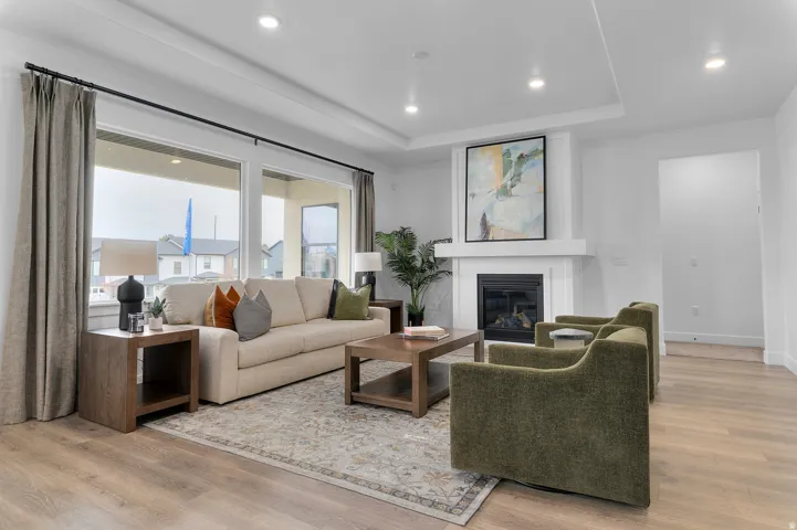 Living area featuring wood-finish flooring, a contemporary fireplace with a white mantel, and large windows with dark curtain rods