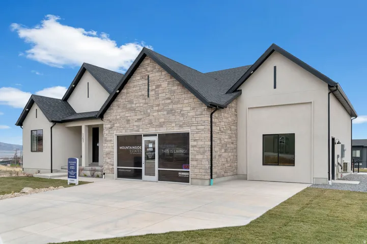 Contemporary exterior featuring a stone and stucco facade, dark-framed windows, a prominent gable roofline, and a concrete driveway