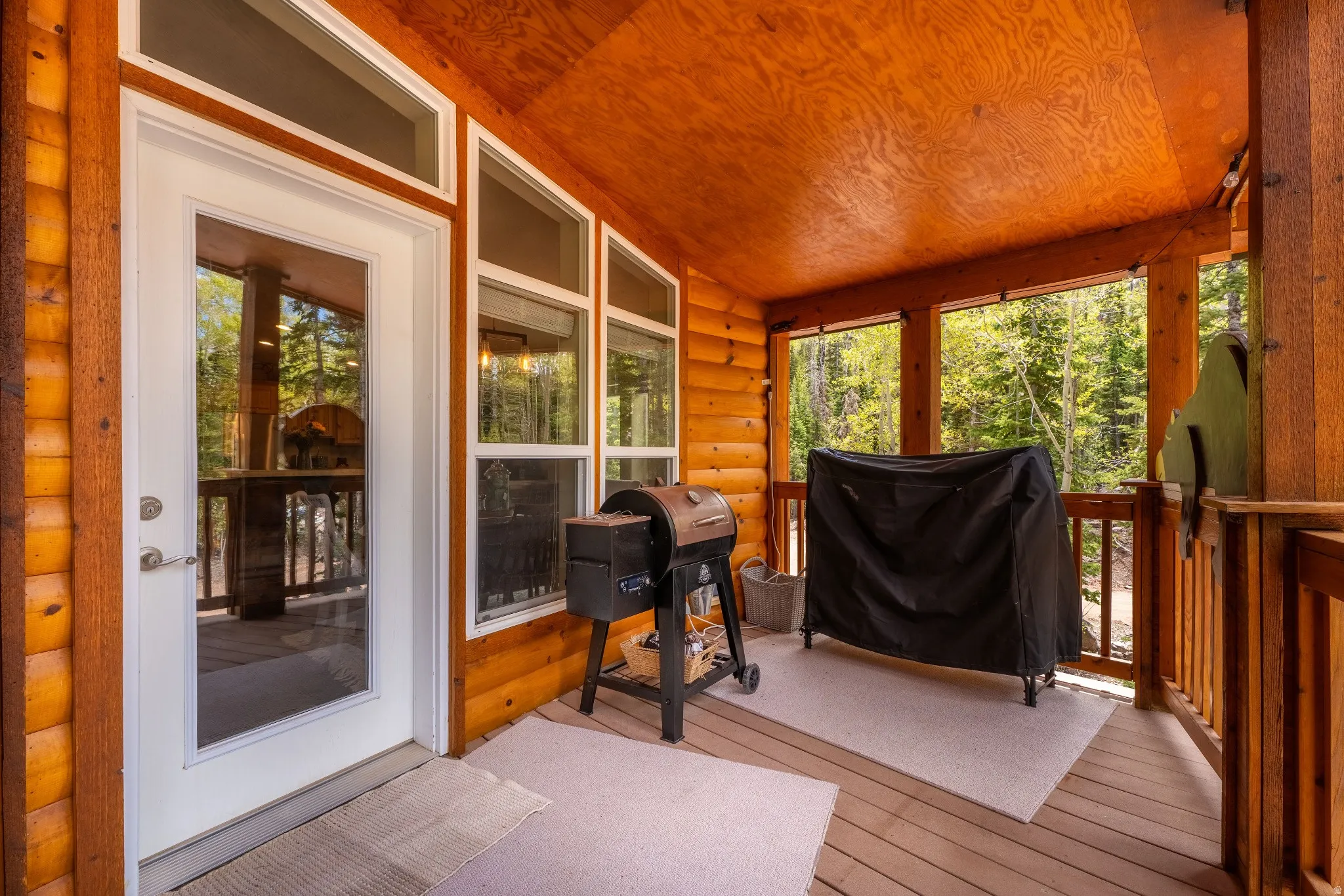 Covered exterior deck featuring exposed wood log construction, light wood-finish flooring, and a glass-paneled exterior door