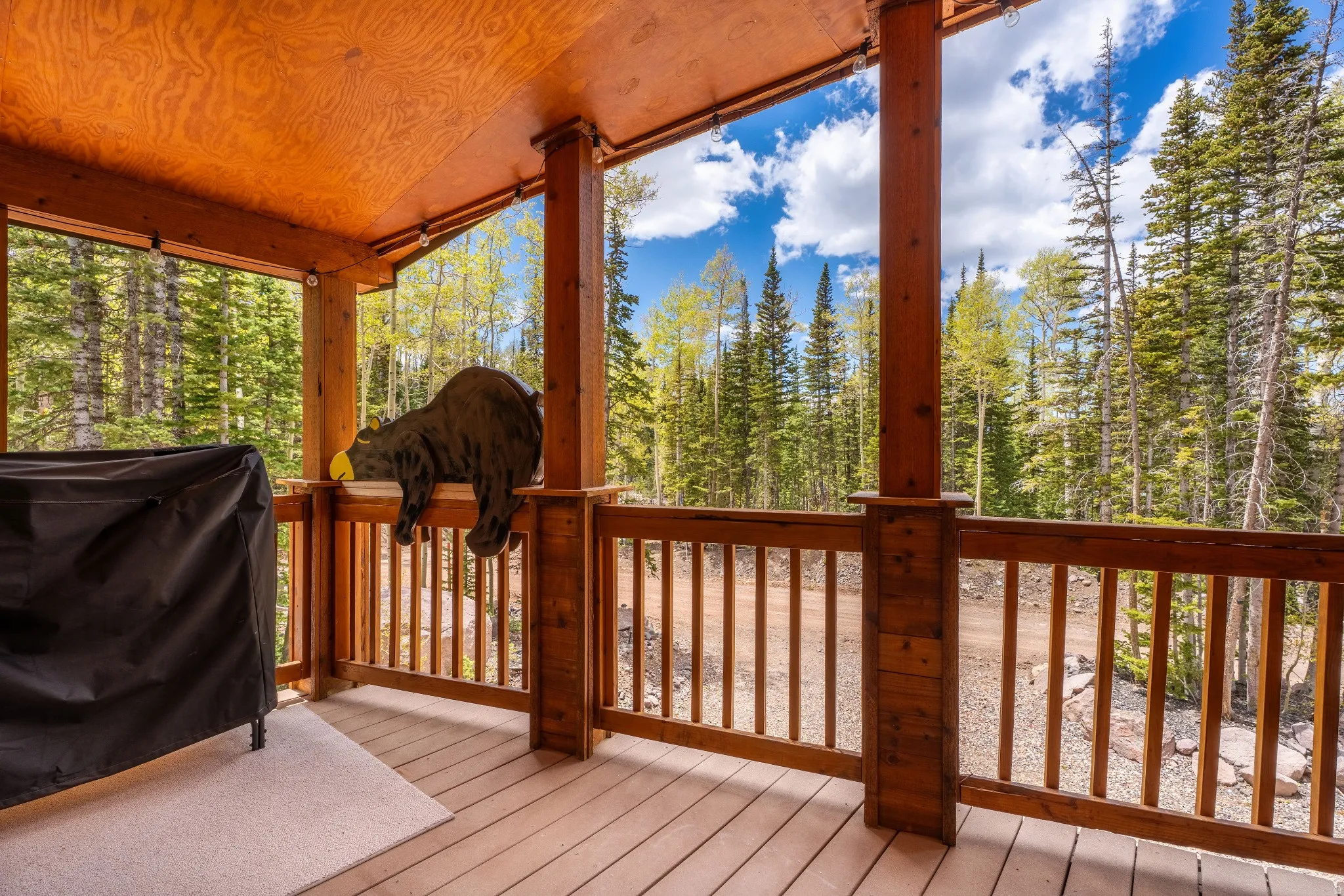 Covered porch with natural wood plank decking, exposed wood ceiling, and wooden railing