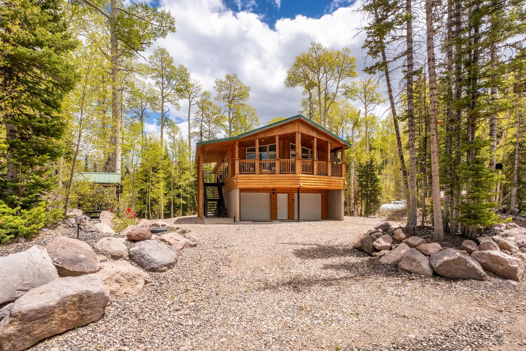 Wood-sided home featuring a covered porch, multiple garage bays, and a gravel driveway