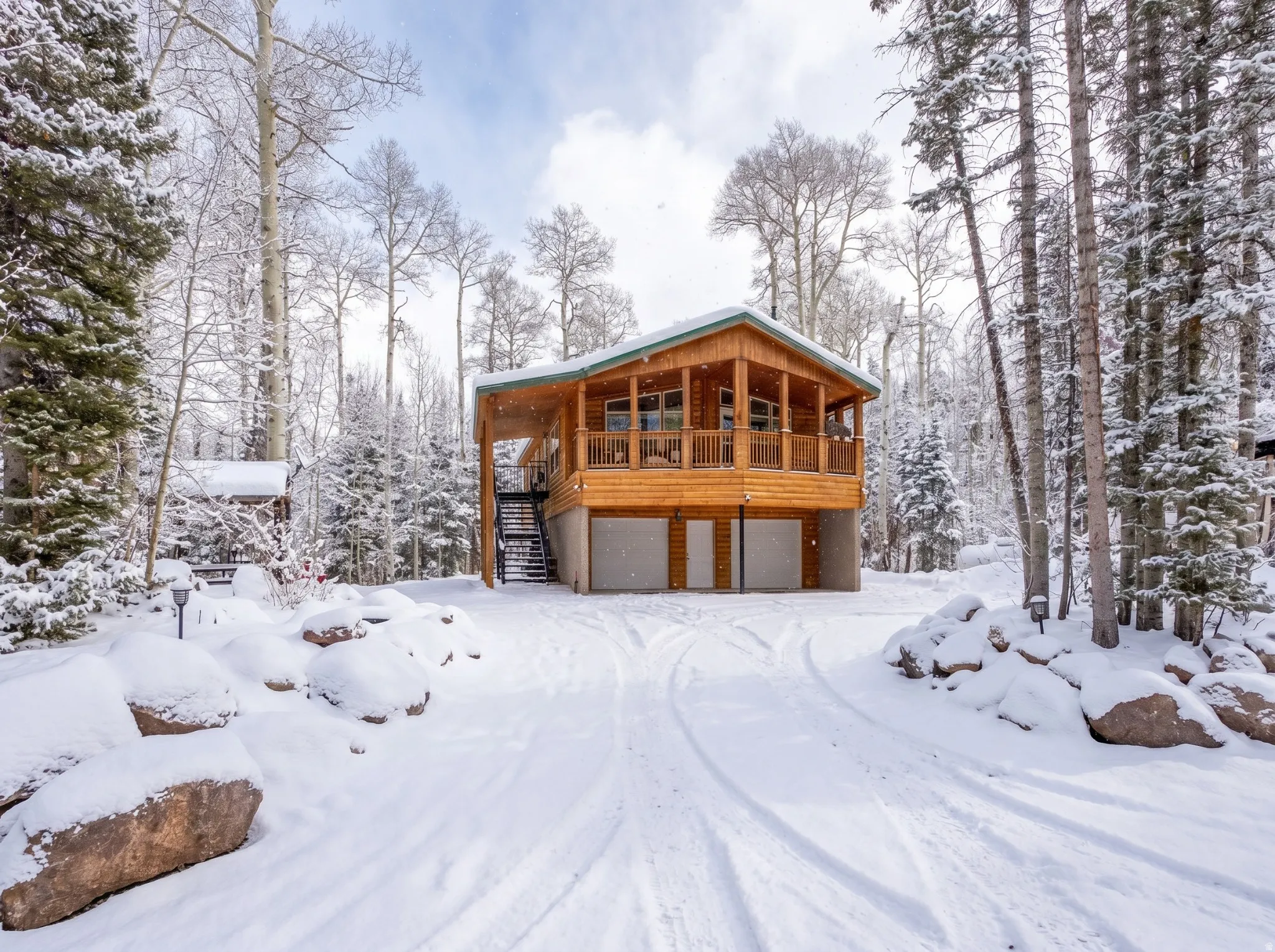 Wood-sided cabin-style residence featuring a covered upper-level deck, ground-level two-car garage, and an exterior staircase