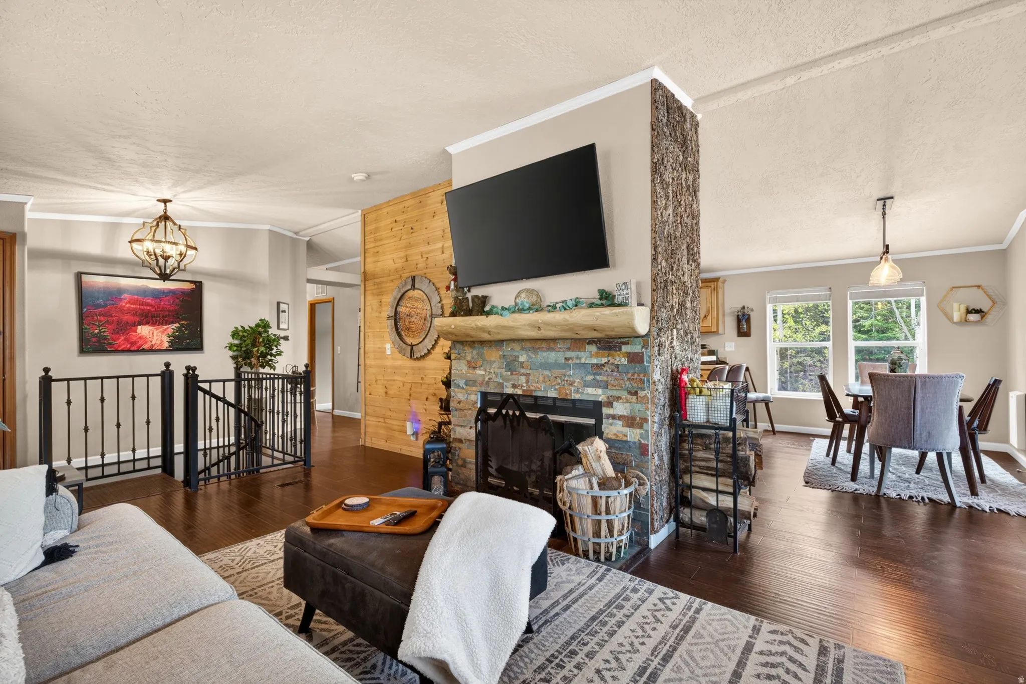 Living area featuring a stone-clad fireplace with a log mantel, rich wood-finish flooring, and a decorative wood-paneled accent wall