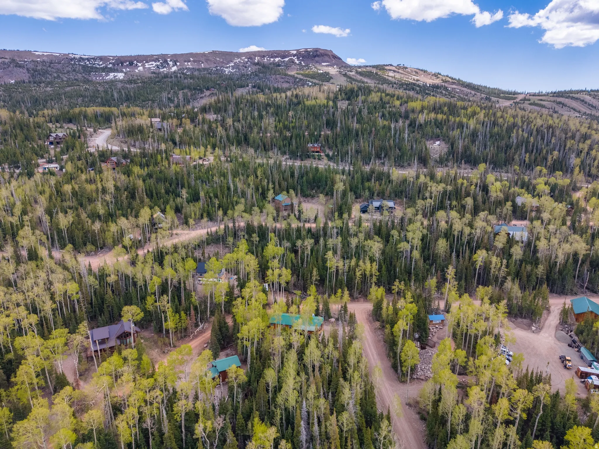 Mountainous terrain featuring dense evergreen and deciduous trees, with scattered residential structures visible among the foliage