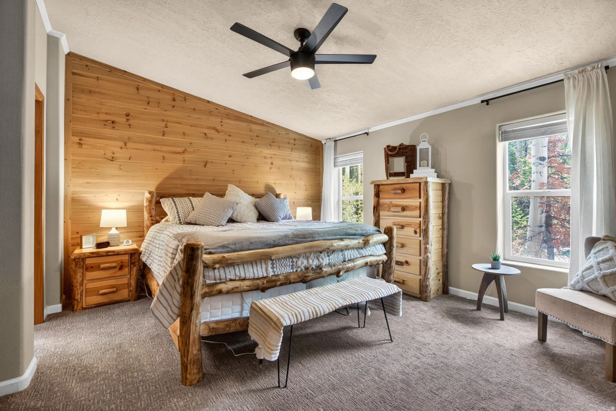 Angled wood-paneled accent wall, neutral wall paint, two double-hung windows, ceiling fan with integrated lighting, and textured carpet flooring