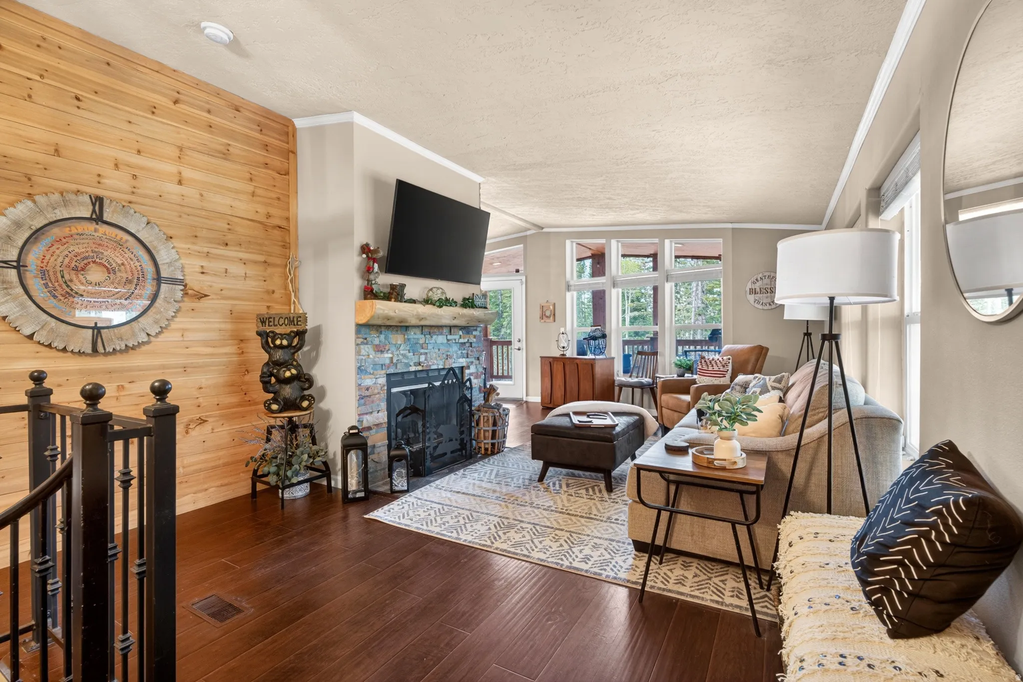 Living area featuring a stone fireplace with a wood mantle, wood-finish flooring, a natural wood accent wall, and large windows