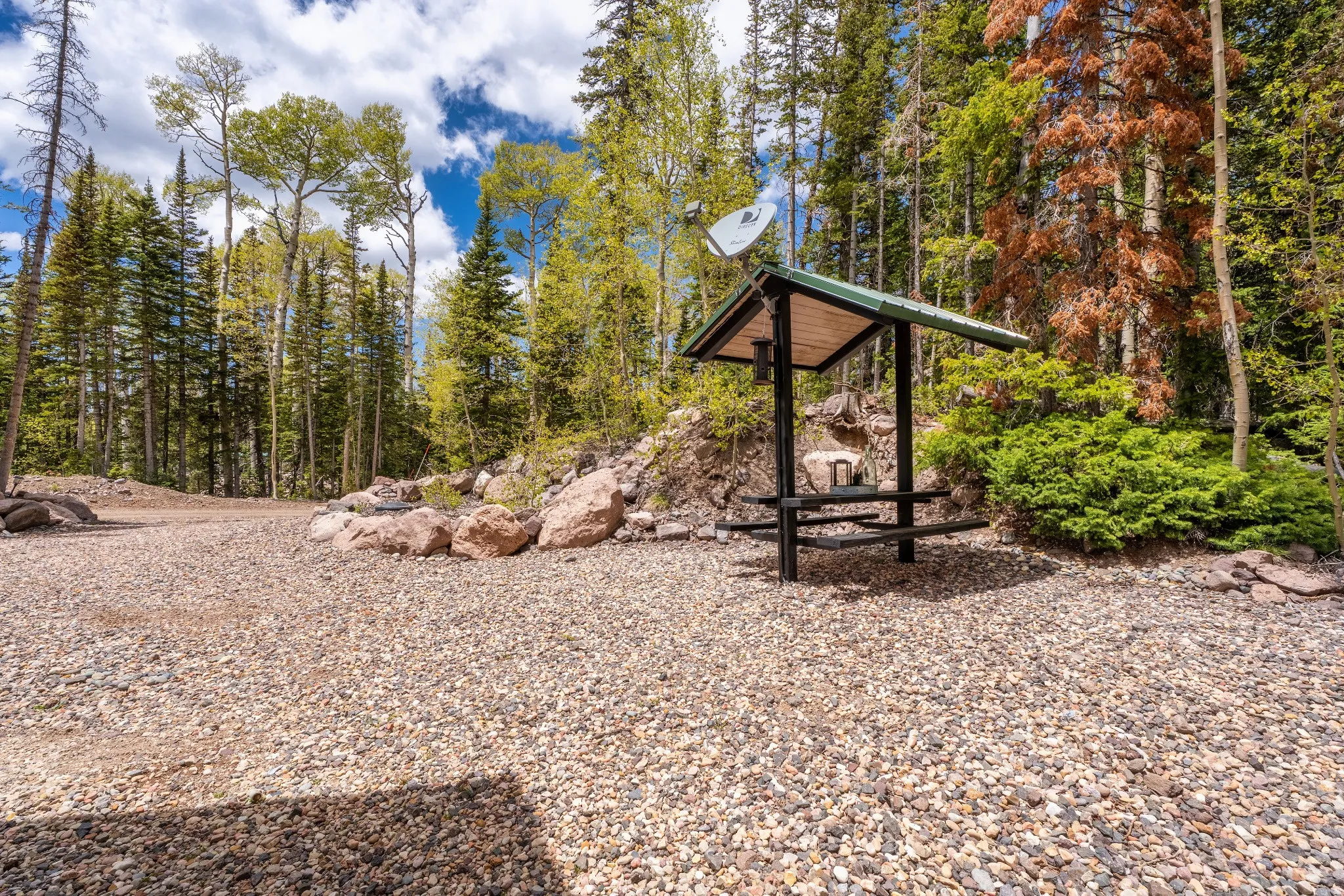 Covered picnic area with a dark green metal roof, set on a gravel surface