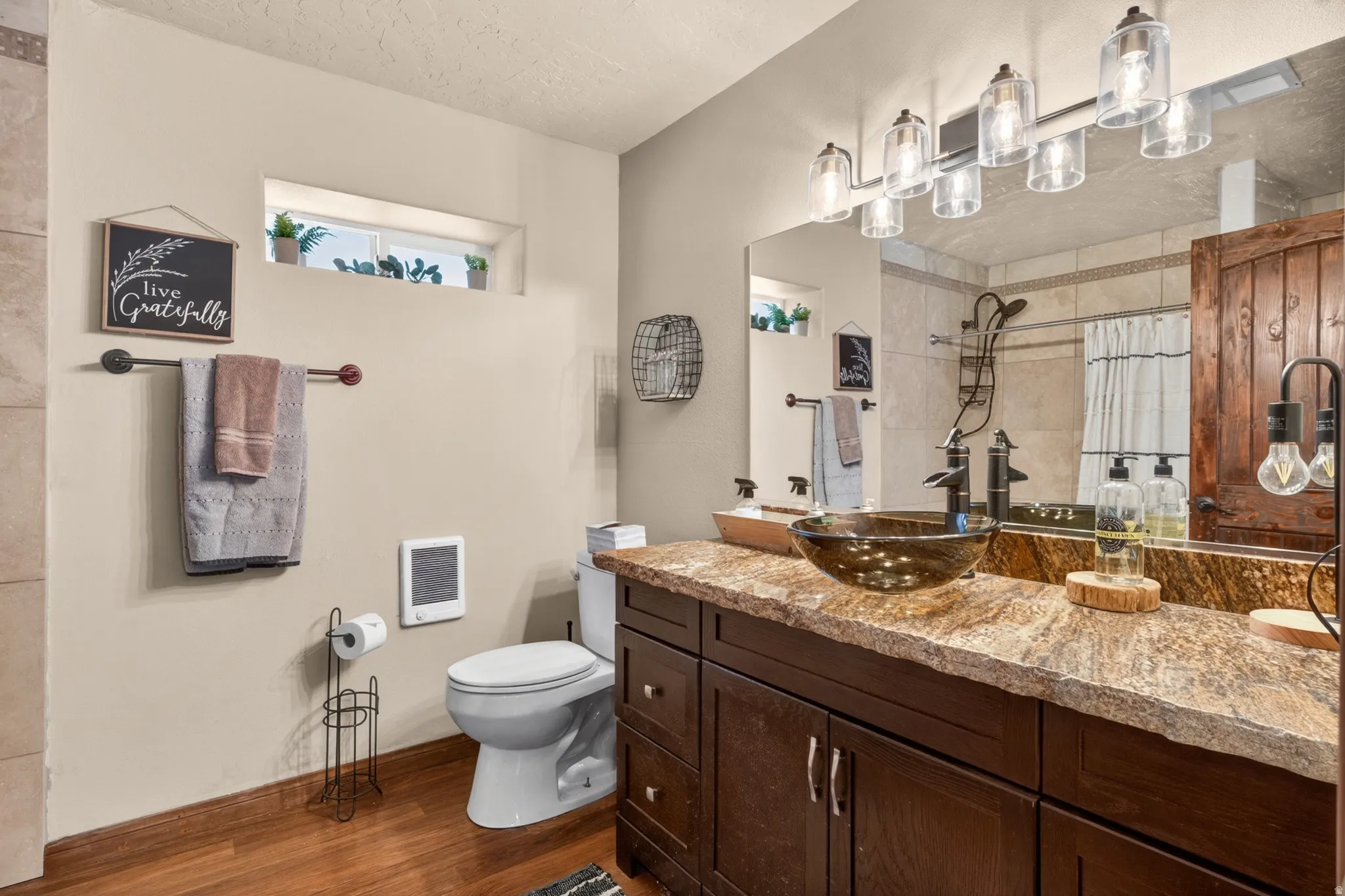 Bathroom featuring a dark wood-finish vanity with a vessel sink, a stone-finish countertop, and a large mirror