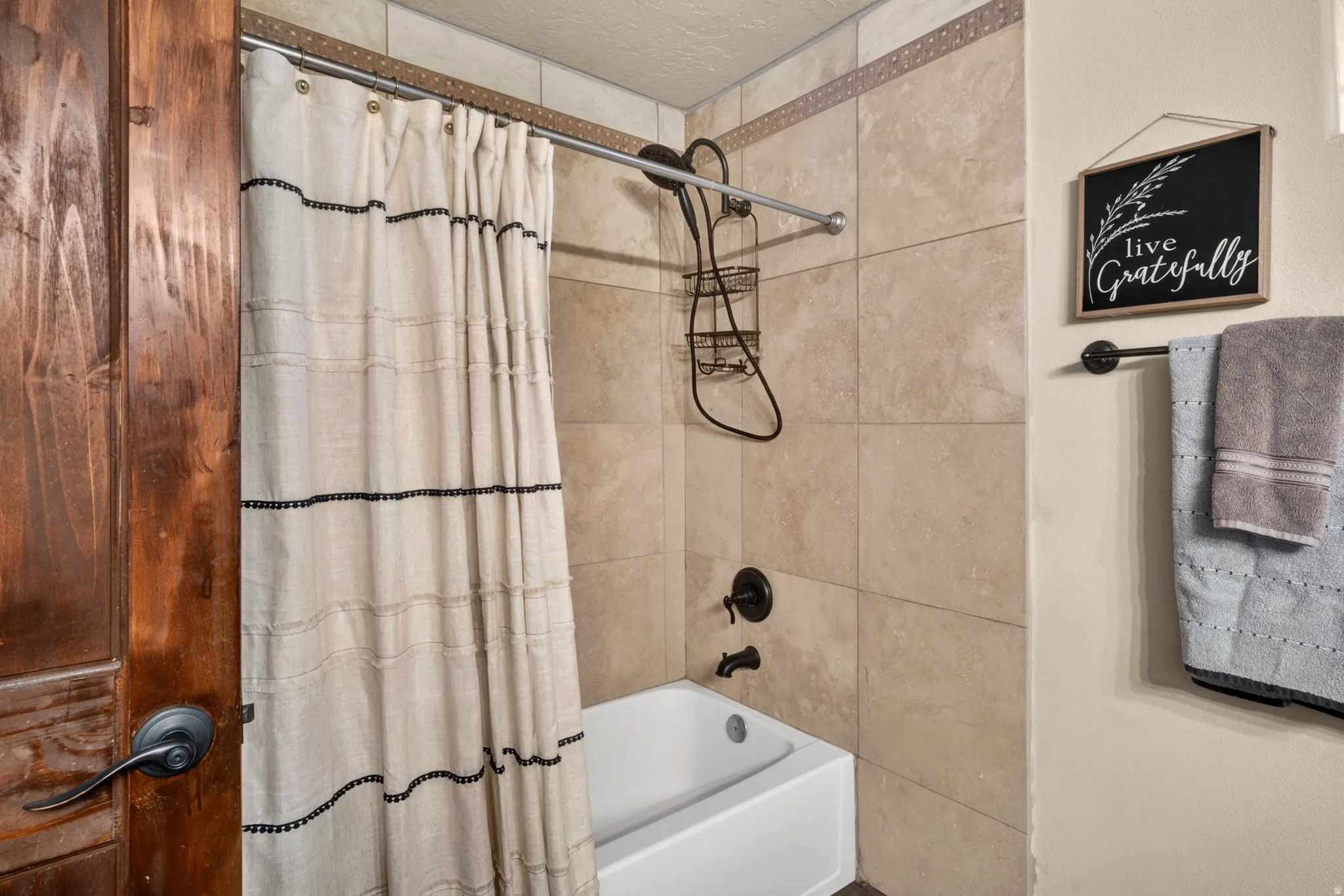 Bathtub and shower combination featuring neutral-toned tile surround with a decorative accent border and matte black fixtures