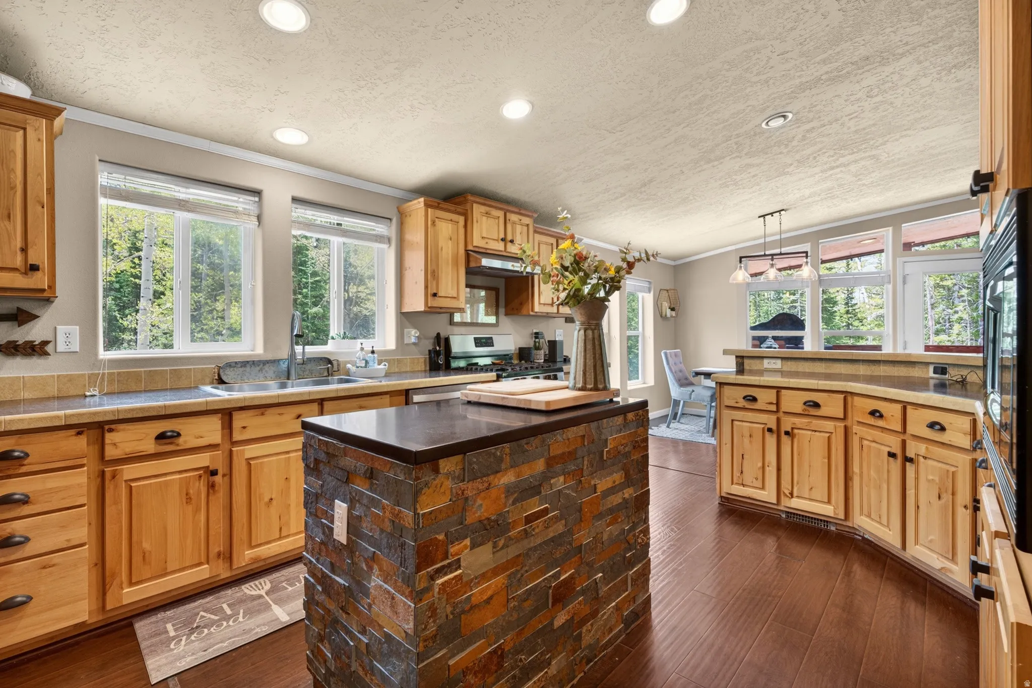 Kitchen featuring wood cabinetry, stone countertops, a stacked stone island, and wood-finish flooring