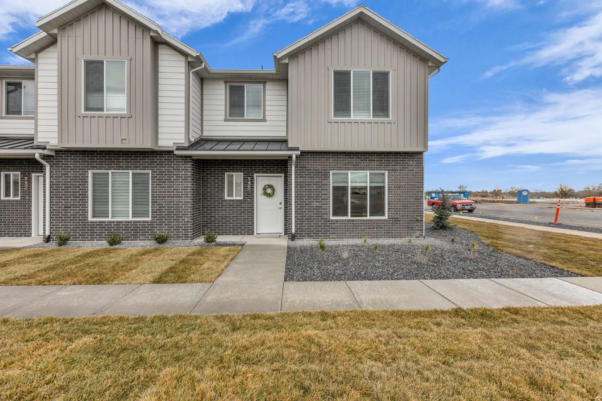 Contemporary townhome exterior featuring a white entry door with frosted glass, dark brick siding, light vertical and horizontal siding accents, and a covered entry