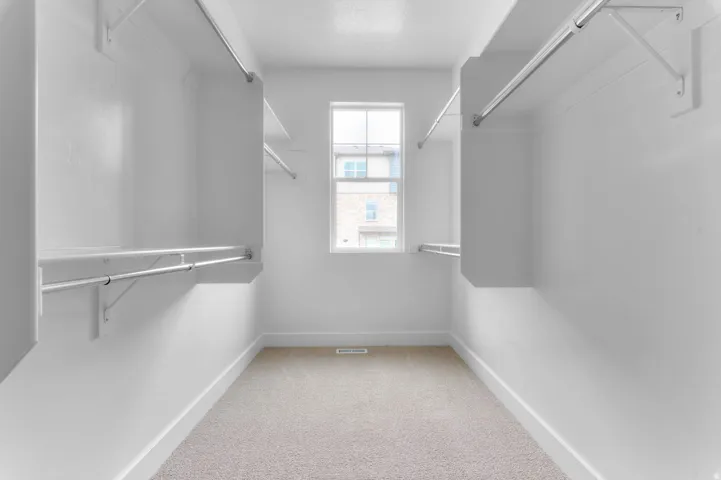 Walk-in closet featuring light-colored carpeting, white walls, multiple hanging rods, built-in shelving, and a prominent window