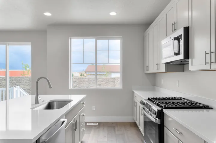 Modern kitchen featuring light gray cabinetry, white countertops, stainless steel appliances, and wood-finish flooring