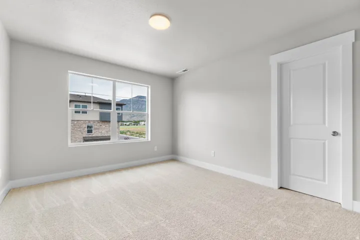 Neutral-toned carpeted room featuring a large window, white trim, a flush mount ceiling light, and a two-panel interior door with a brushed nickel knob