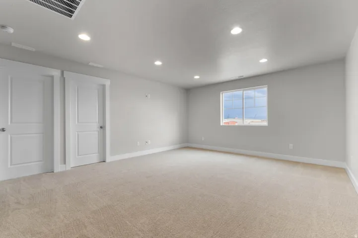 Spacious room featuring neutral carpeting, light gray walls, recessed lighting, white baseboards, and a large window