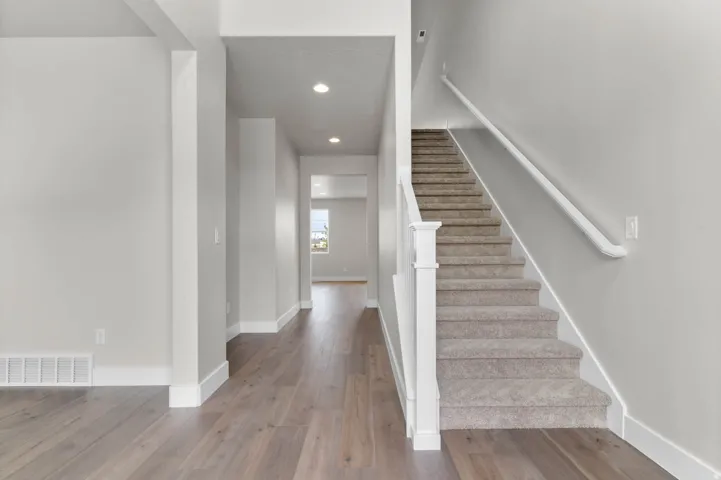 Inviting entryway featuring wood-finish flooring, a carpeted staircase with white newel post, and recessed lighting