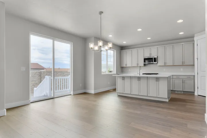 Open-concept kitchen and dining area featuring wide plank wood-finish flooring, light gray cabinetry, a central island with an undermount sink, stainless steel appliances, and a sliding glass door providing exterior access