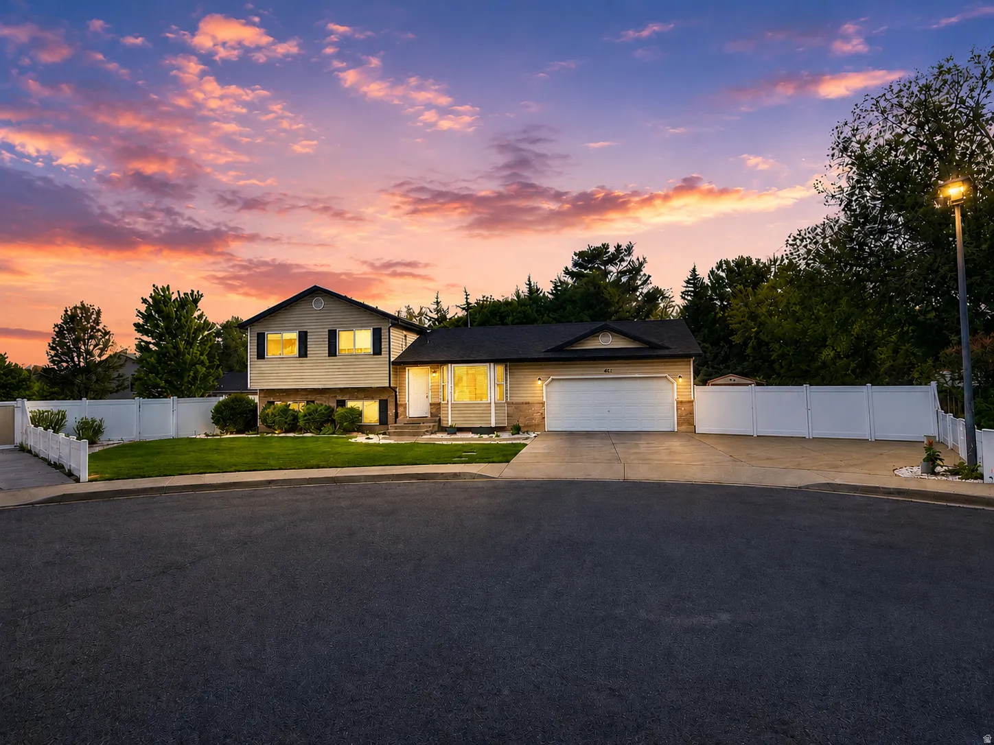Split-level residence featuring a two-car garage, mature landscaping, and a fenced perimeter