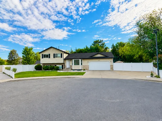 Split-level residence featuring a two-car garage, concrete driveway, and a white vinyl fence enclosing a portion of the yard