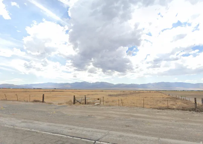 Expansive open landscape featuring a rustic metal gate, post fencing, and distant mountain ranges