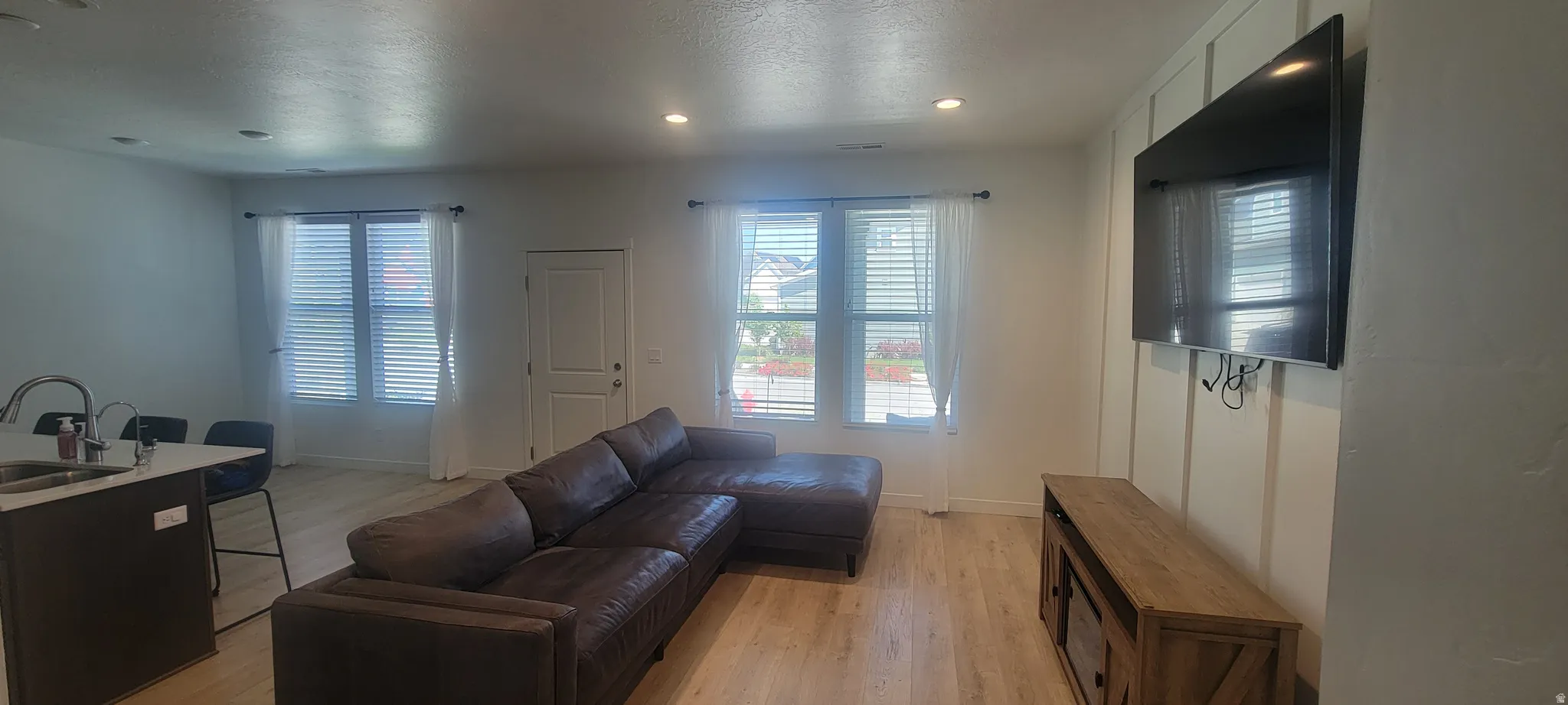 Open-concept living space featuring light wood-finish flooring, recessed lighting, and ample natural light from multiple windows