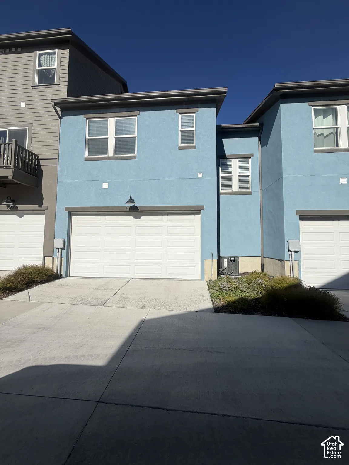 Two-story exterior featuring blue stucco siding, a multi-paneled garage door, dual-pane windows with trim, and a concrete driveway