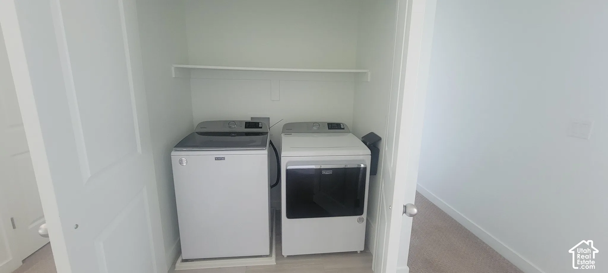 Dedicated laundry closet with overhead shelving, featuring a Maytag washing machine and dryer included with the home