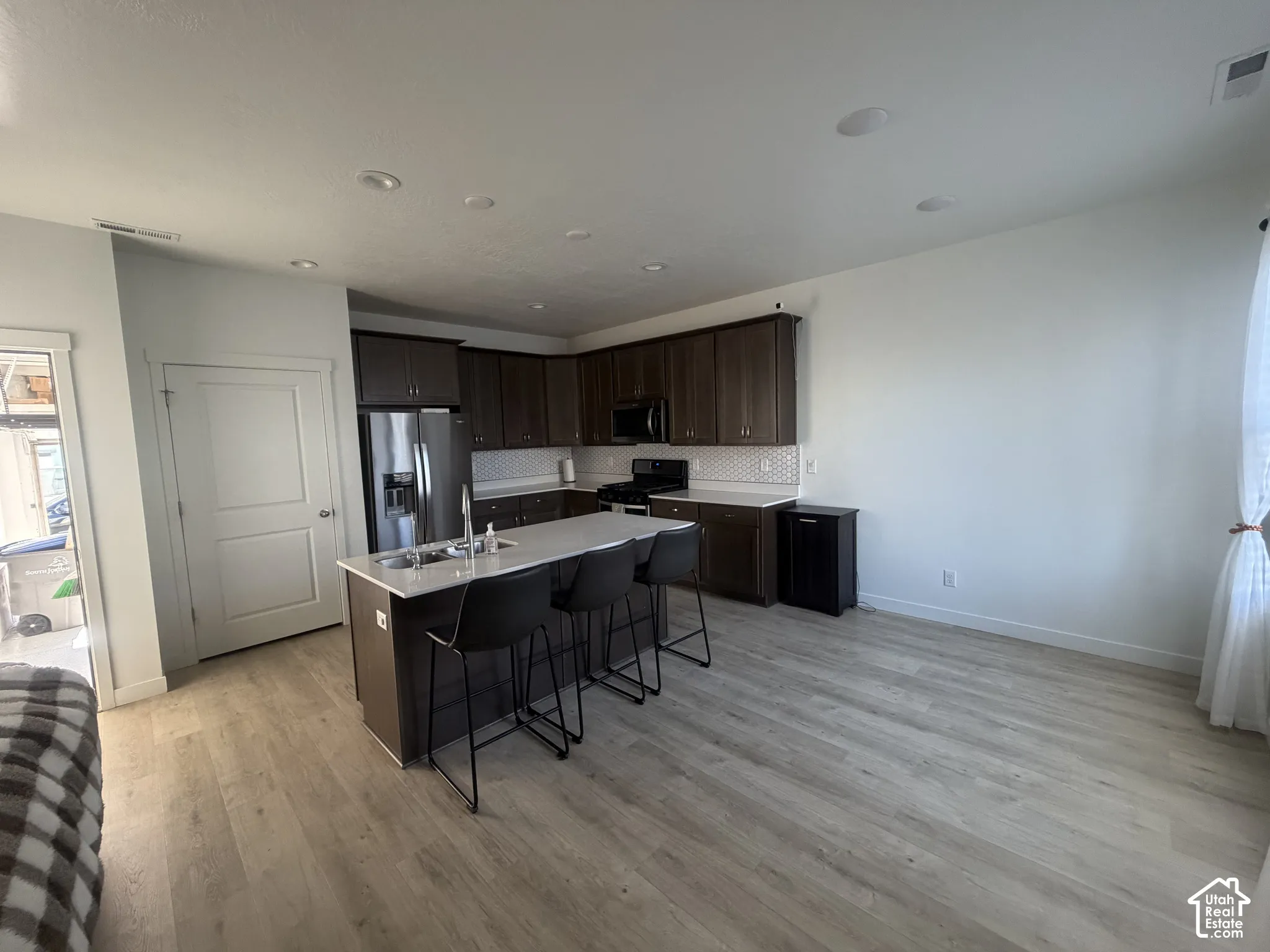 Kitchen featuring dark-finish cabinetry, white countertops, a center island with an undermount stainless steel sink, wood-finish flooring, and recessed ceiling lighting