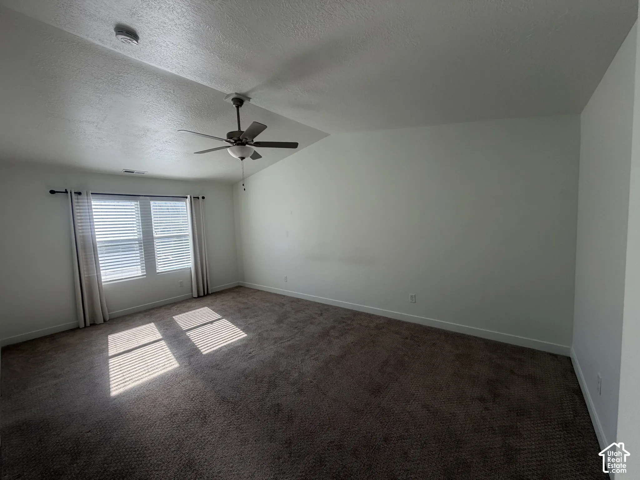 Room featuring vaulted ceilings, neutral carpeting, and a multi-blade ceiling fan with an integrated light fixture