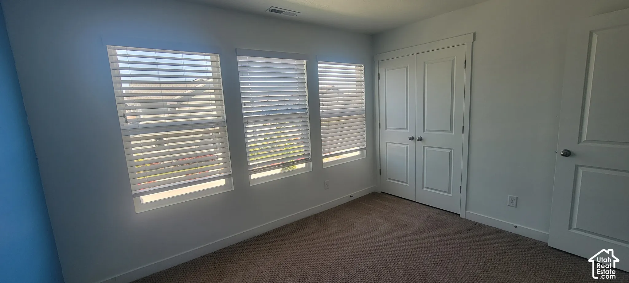 bedroom 2 featuring three vertical windows with horizontal blinds, carpeted flooring, and a pair of white bifold closet doors