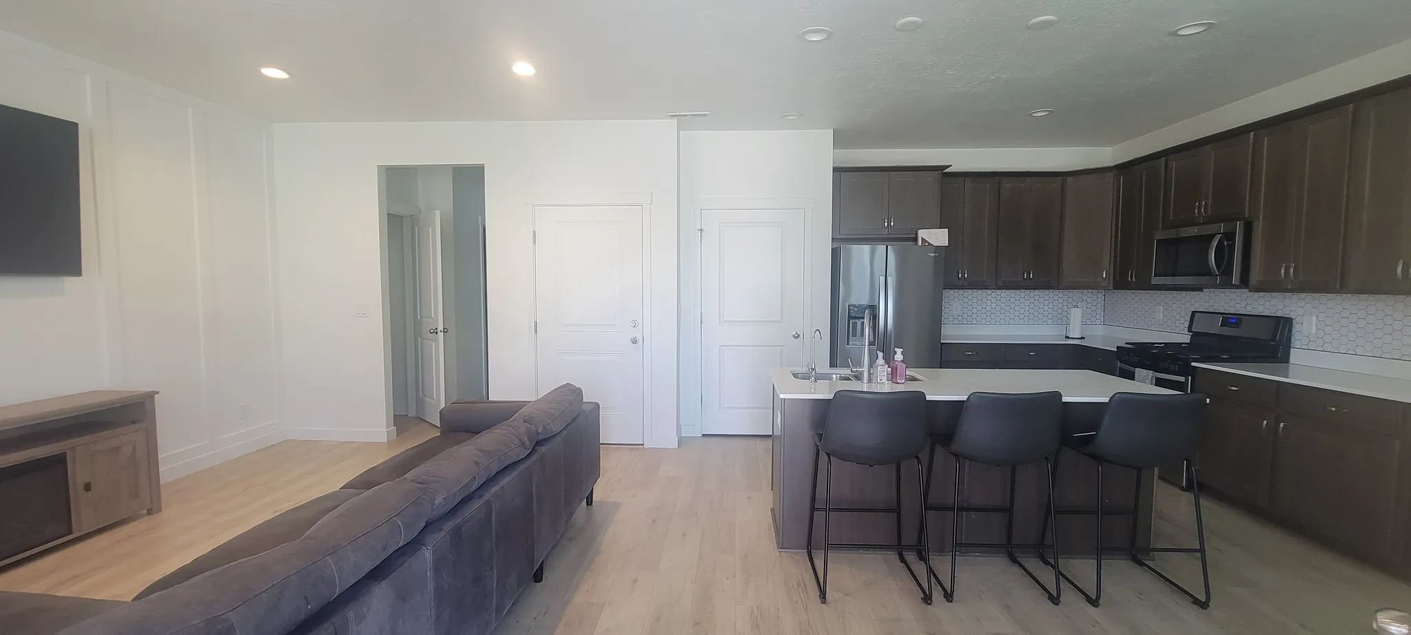 Open-concept living space featuring wood-finish flooring, recessed lighting, a kitchen island with seating, a patterned tile backsplash, and stainless steel appliances