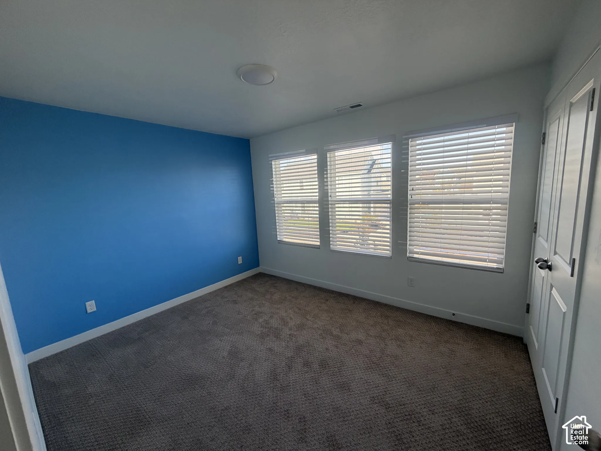 Neutral-toned interior space featuring wall-to-wall carpeting, three windows with adjustable horizontal blinds, and a built-in closet with six-panel doors