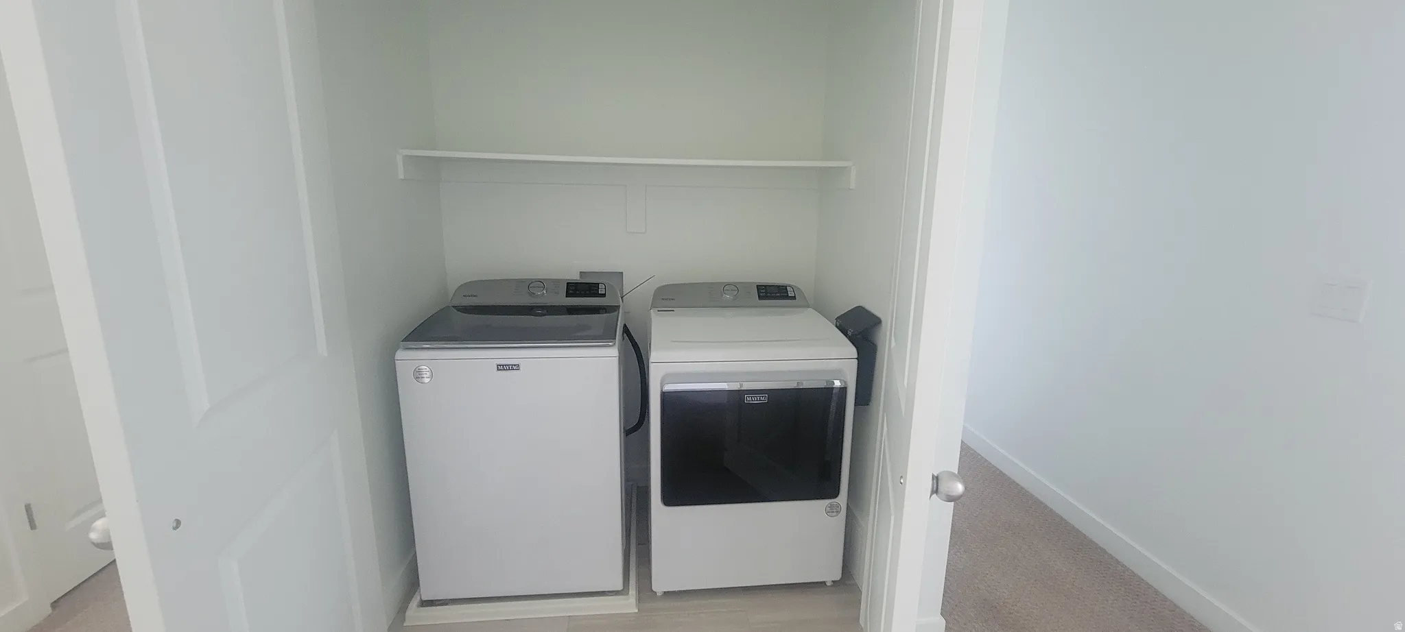 Dedicated laundry closet with overhead shelving, featuring a Maytag washing machine and dryer included with the home