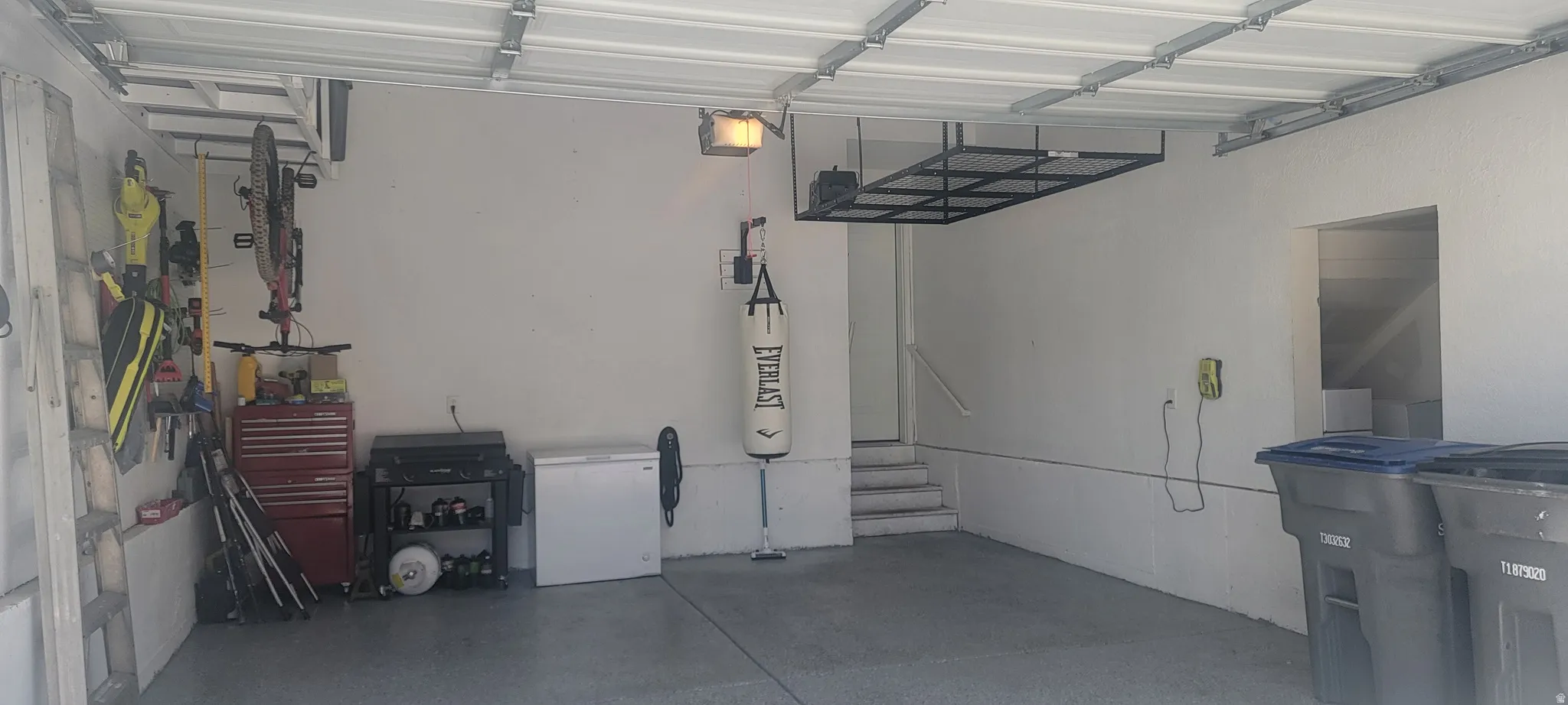Spacious garage featuring a concrete floor, painted walls, overhead storage racks, a utility sink, and interior access via stairs