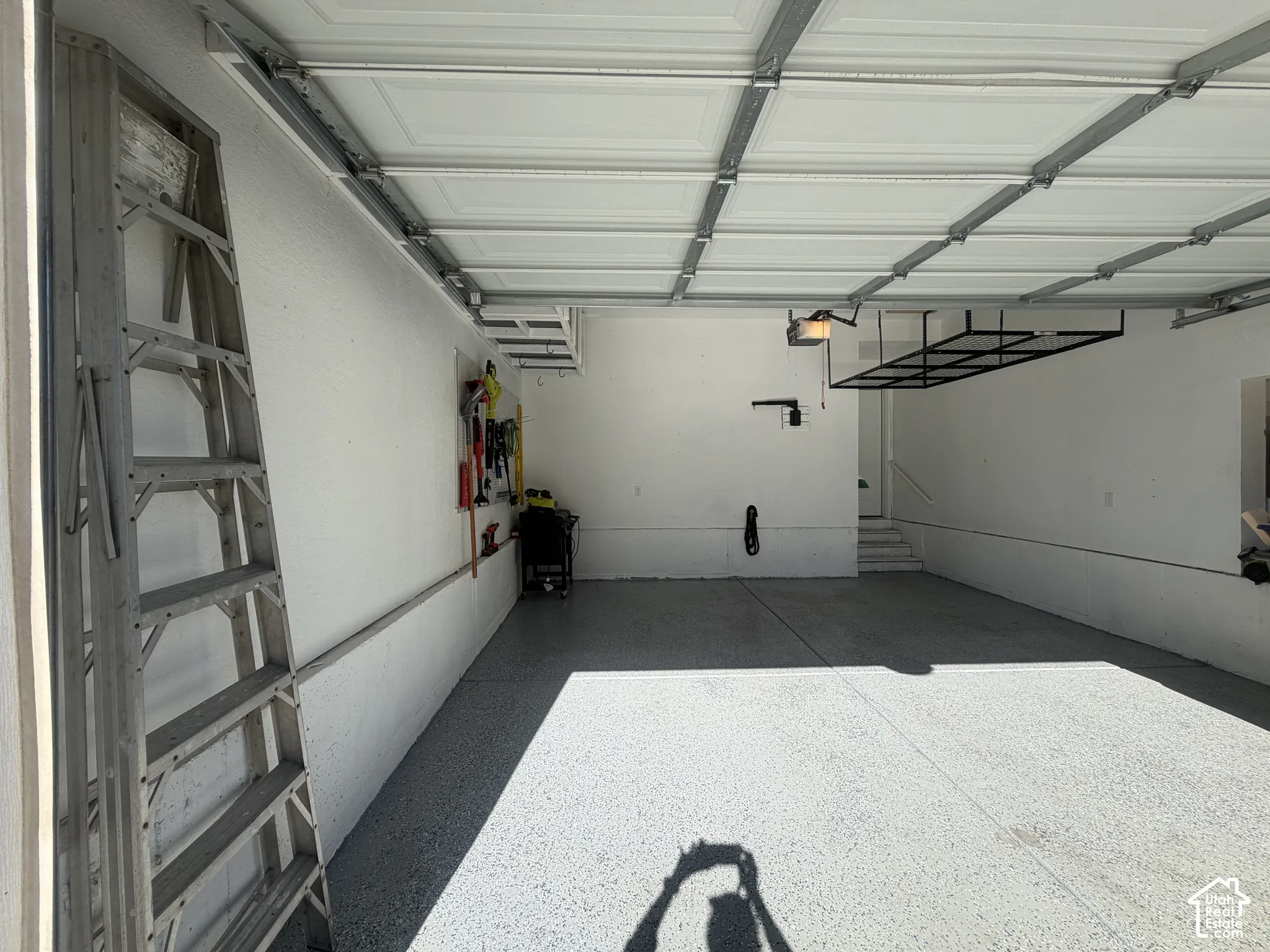 Garage featuring an epoxy-coated floor, white finished walls, overhead track door system, and ceiling-mounted storage rack