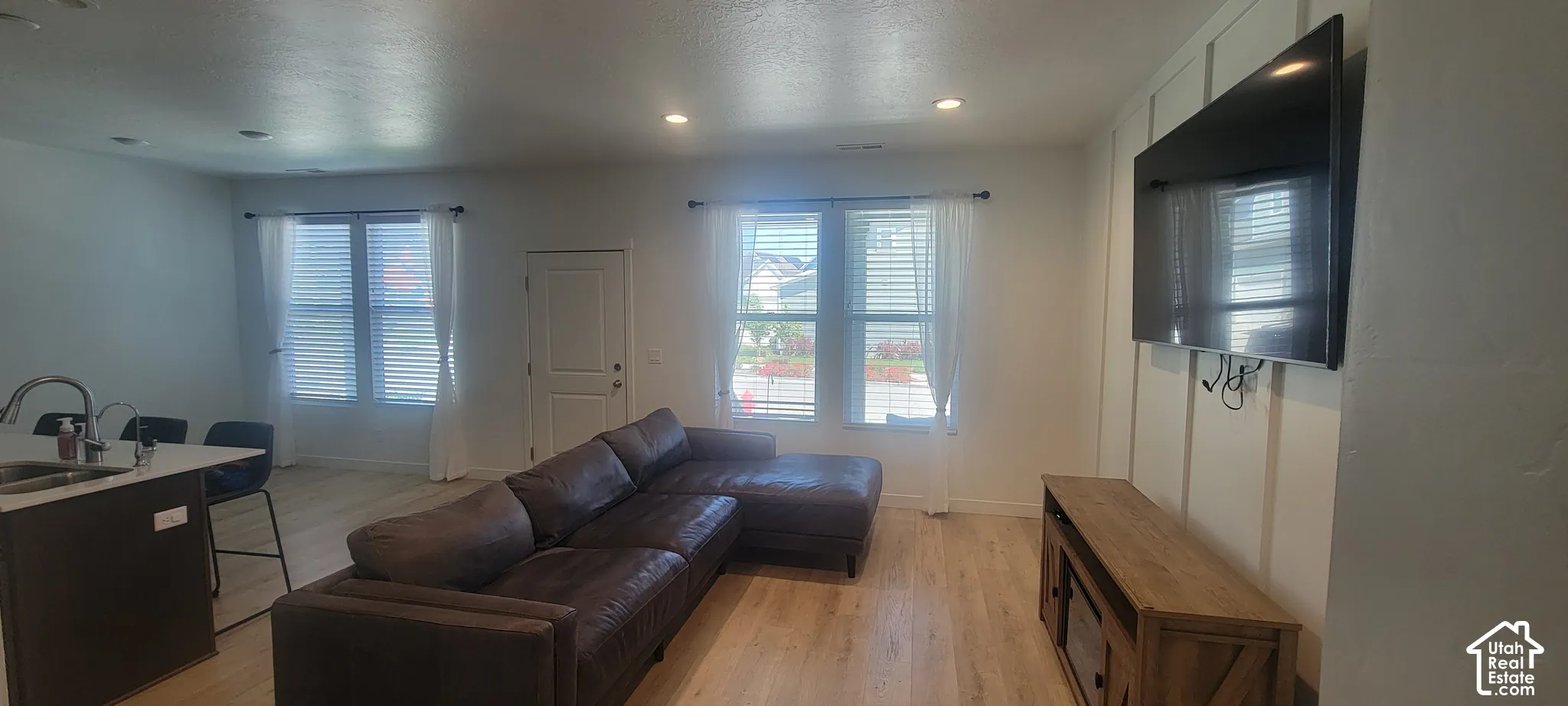 Open-concept living space featuring light wood-finish flooring, recessed lighting, and ample natural light from multiple windows