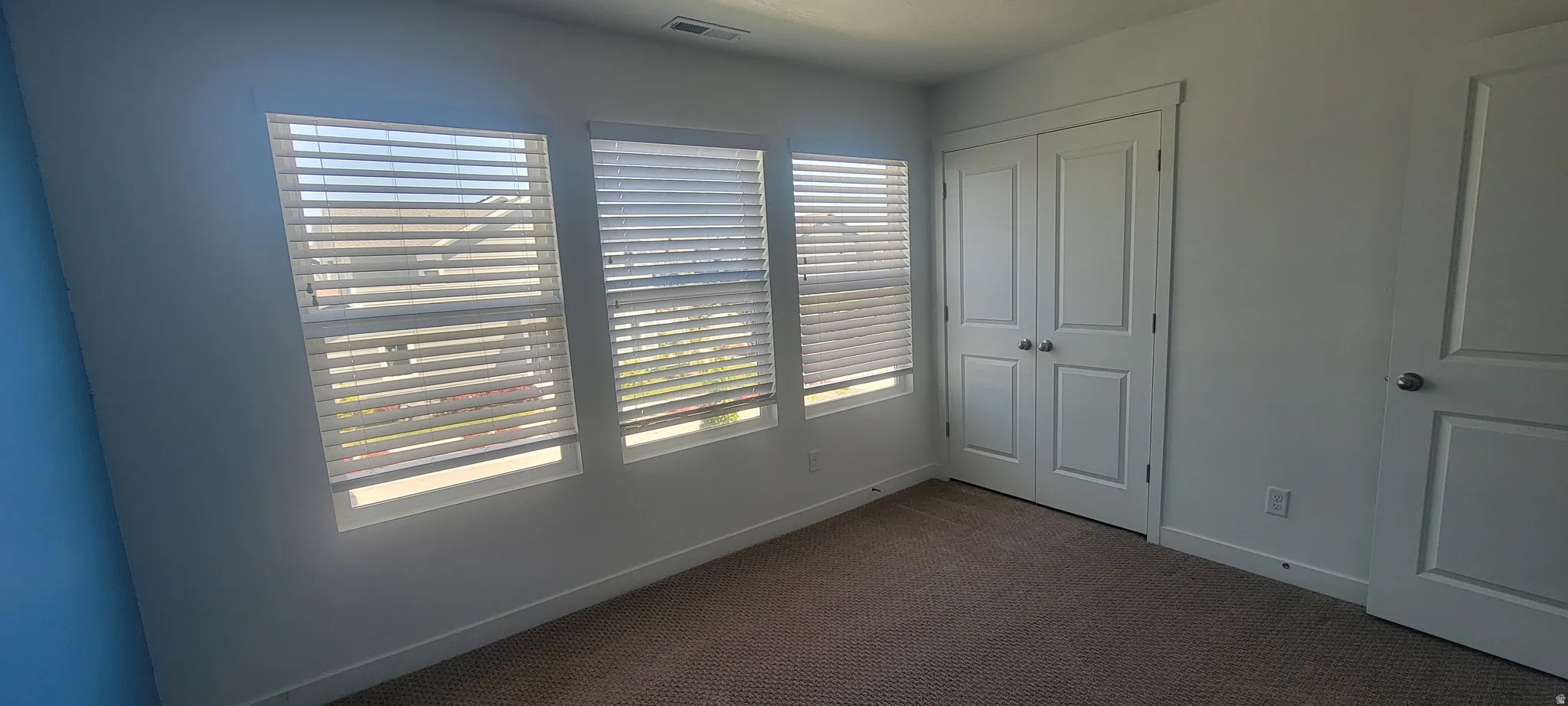 bedroom 2 featuring three vertical windows with horizontal blinds, carpeted flooring, and a pair of white bifold closet doors