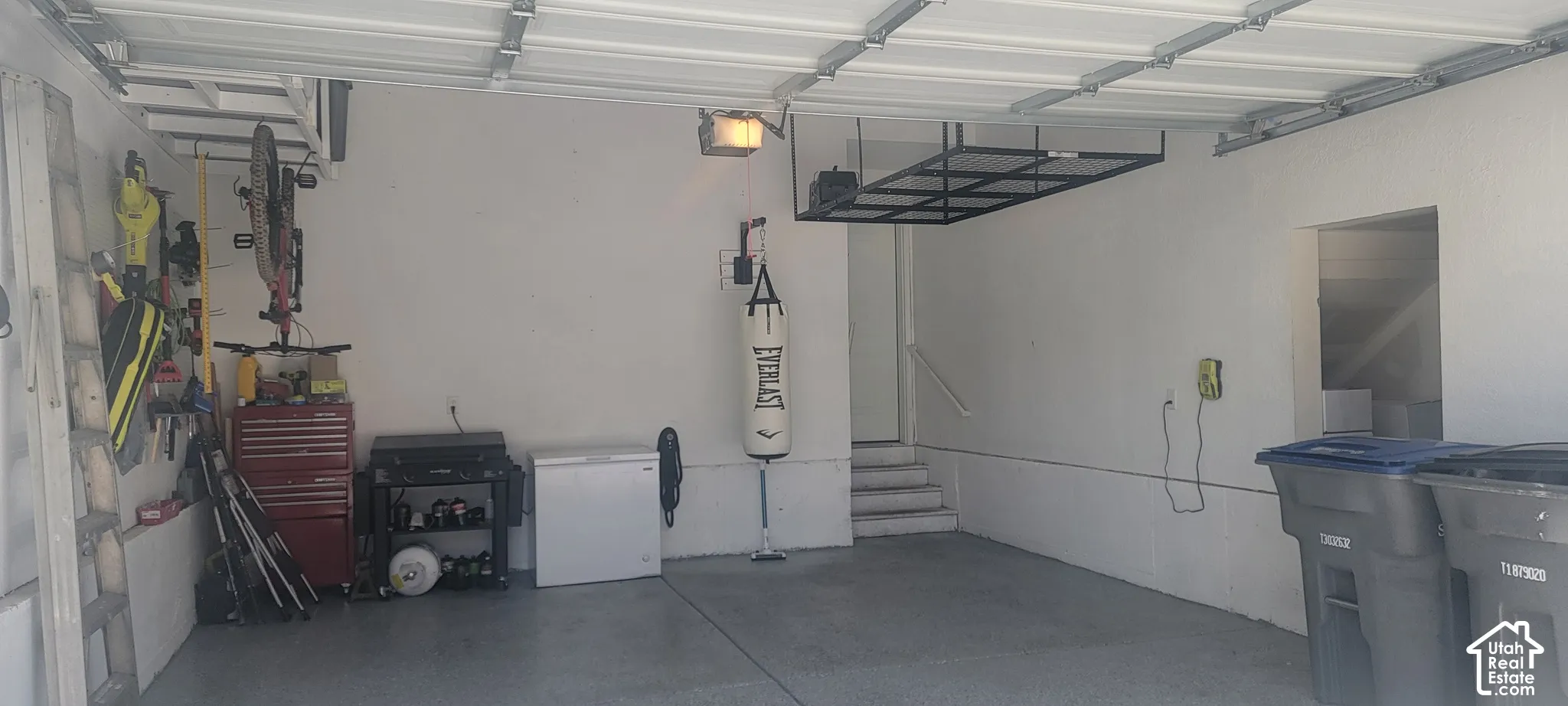 Spacious garage featuring an e concrete floor, painted walls, overhead storage racks, a utility sink, and interior access via stairs
