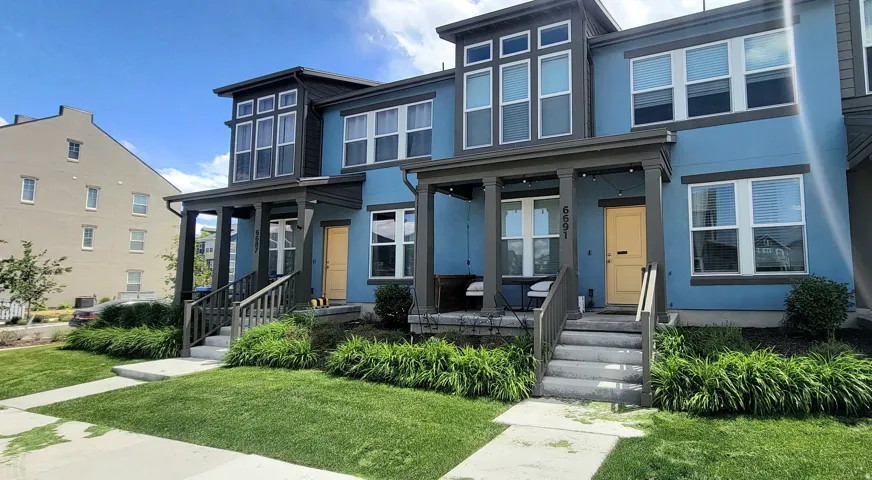 Modern townhome exterior with a distinctive blue facade, contrasting charcoal trim, and a bright yellow front door