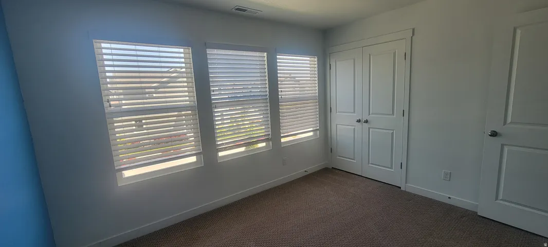 bedroom 2 featuring three vertical windows with horizontal blinds, carpeted flooring, and a pair of white bifold closet doors