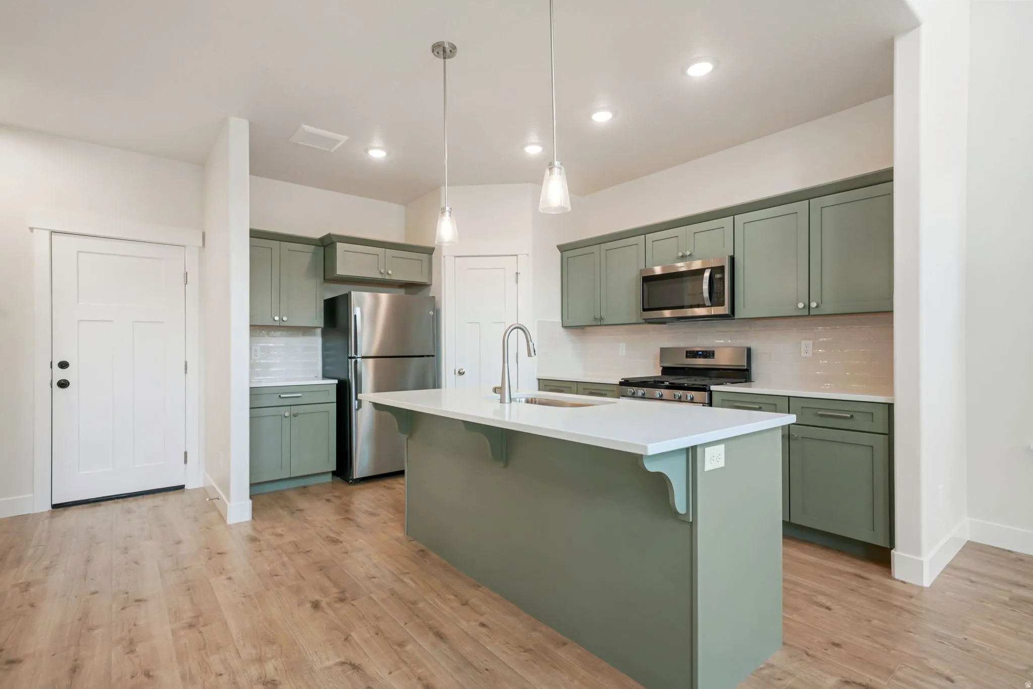 Kitchen featuring sage green cabinetry, stainless steel appliances, a white subway tile backsplash, and light wood-finish flooring