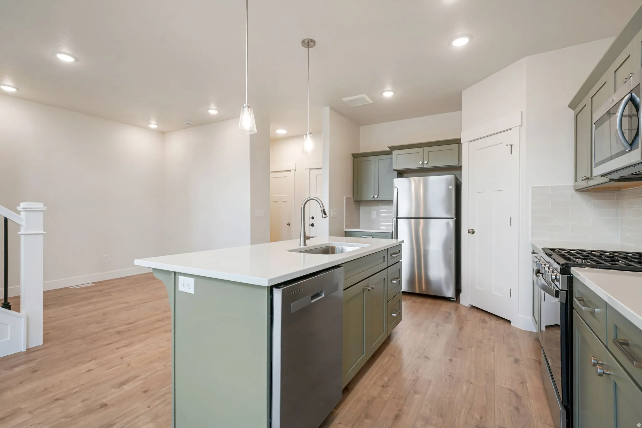 Open-concept kitchen featuring an island with integrated sink, stainless steel appliances, light wood-finish flooring, recessed lighting, and pendant lighting fixtures