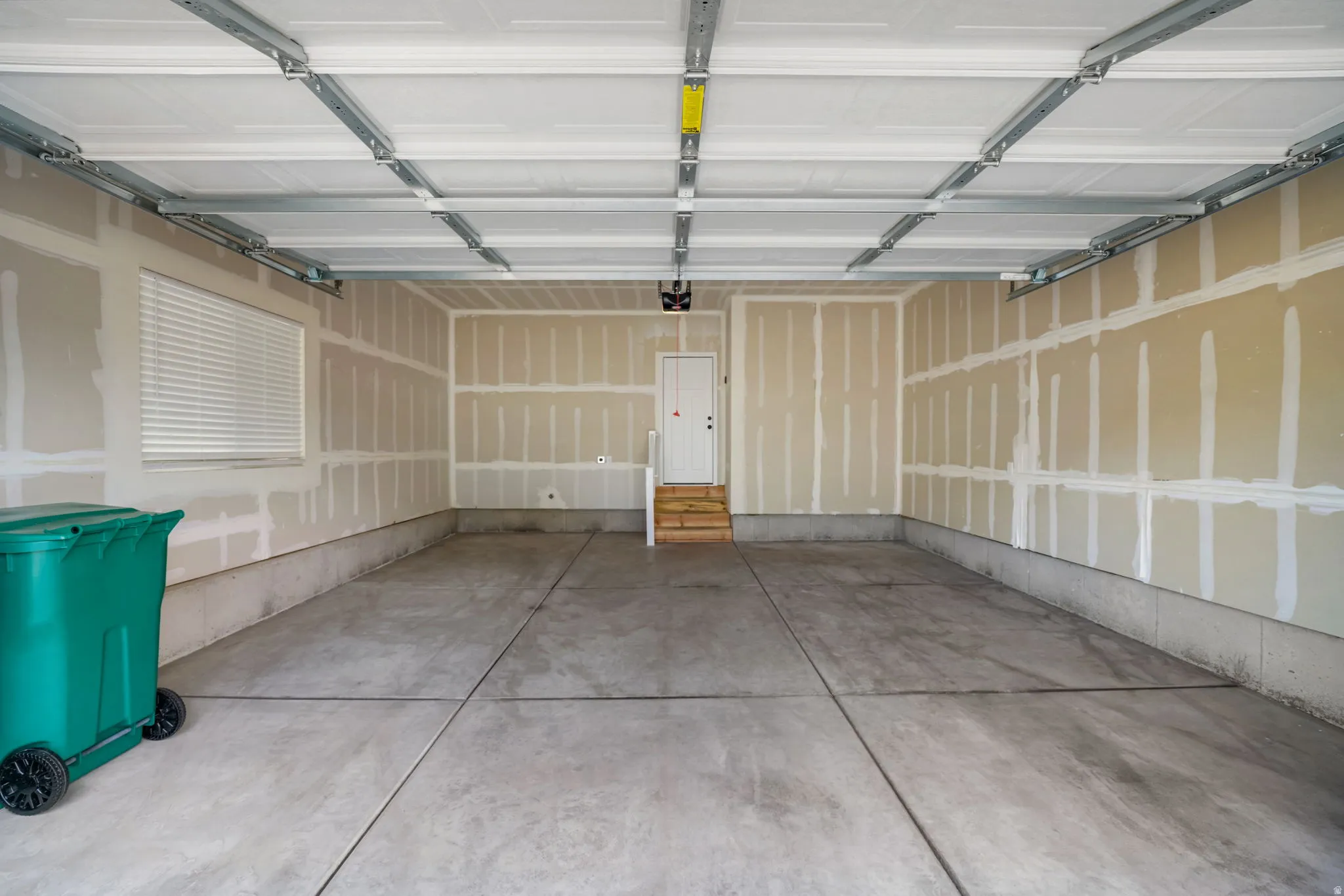 Spacious two-car garage featuring a concrete floor, window with blinds, and interior access door with wooden steps