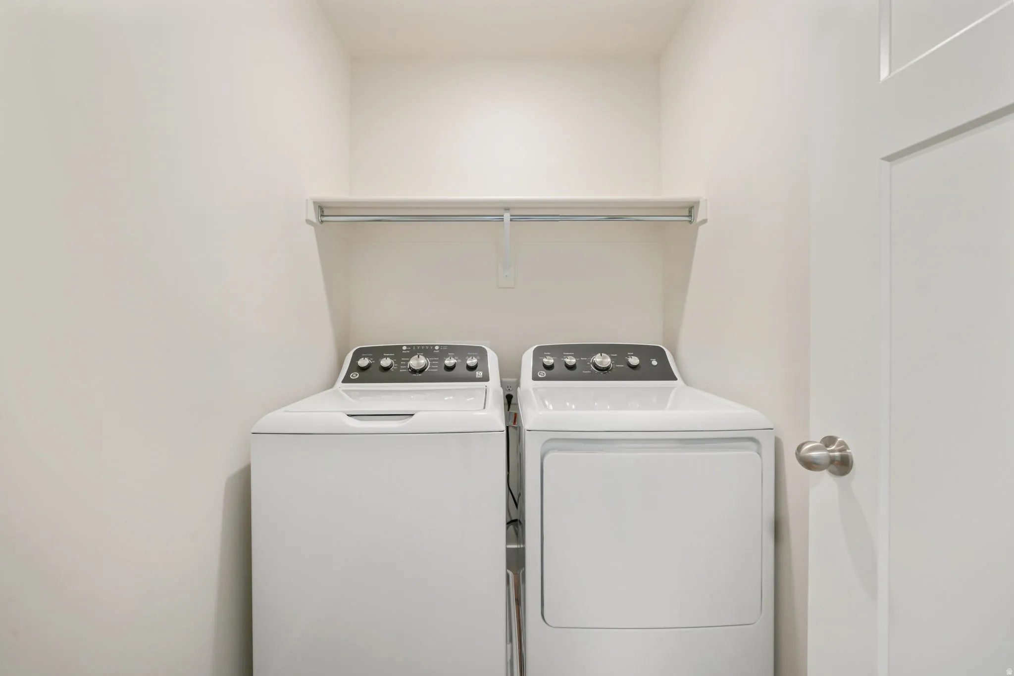 Laundry area featuring a top-load washing machine, front-load dryer, and an upper storage shelf with a hanging rod