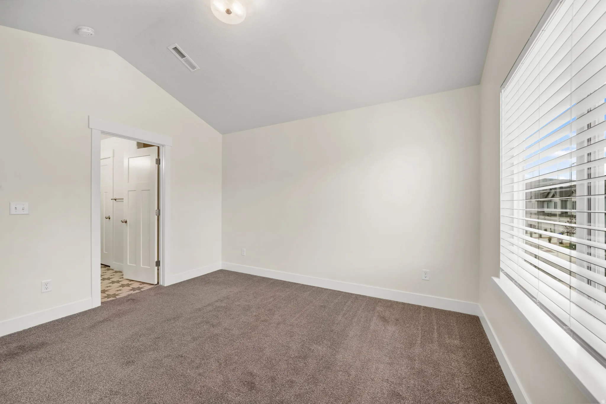Carpeted room featuring a vaulted ceiling and a large window with blinds