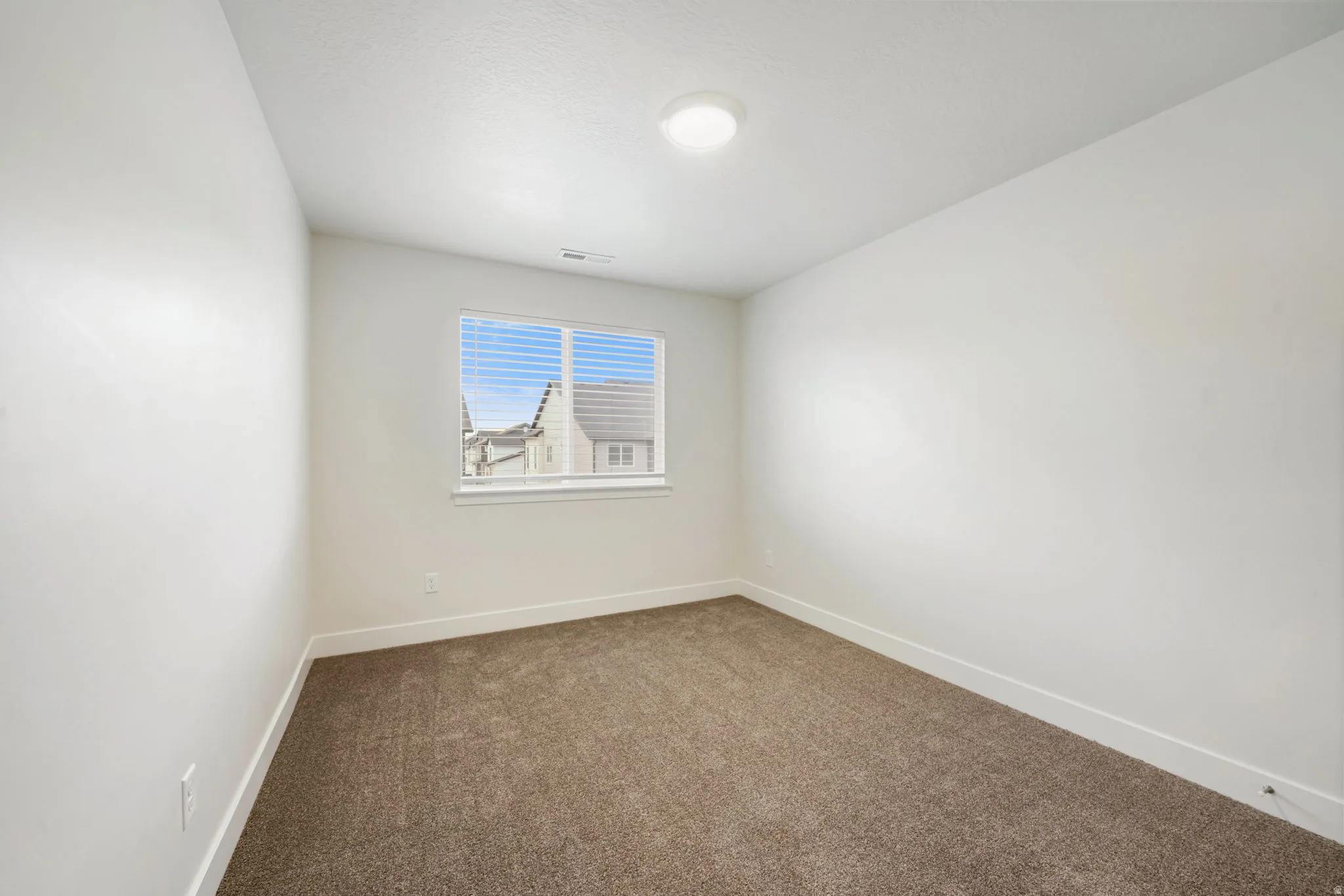 Neutral tone wall finishes, brown carpet flooring, and a single window with horizontal blinds