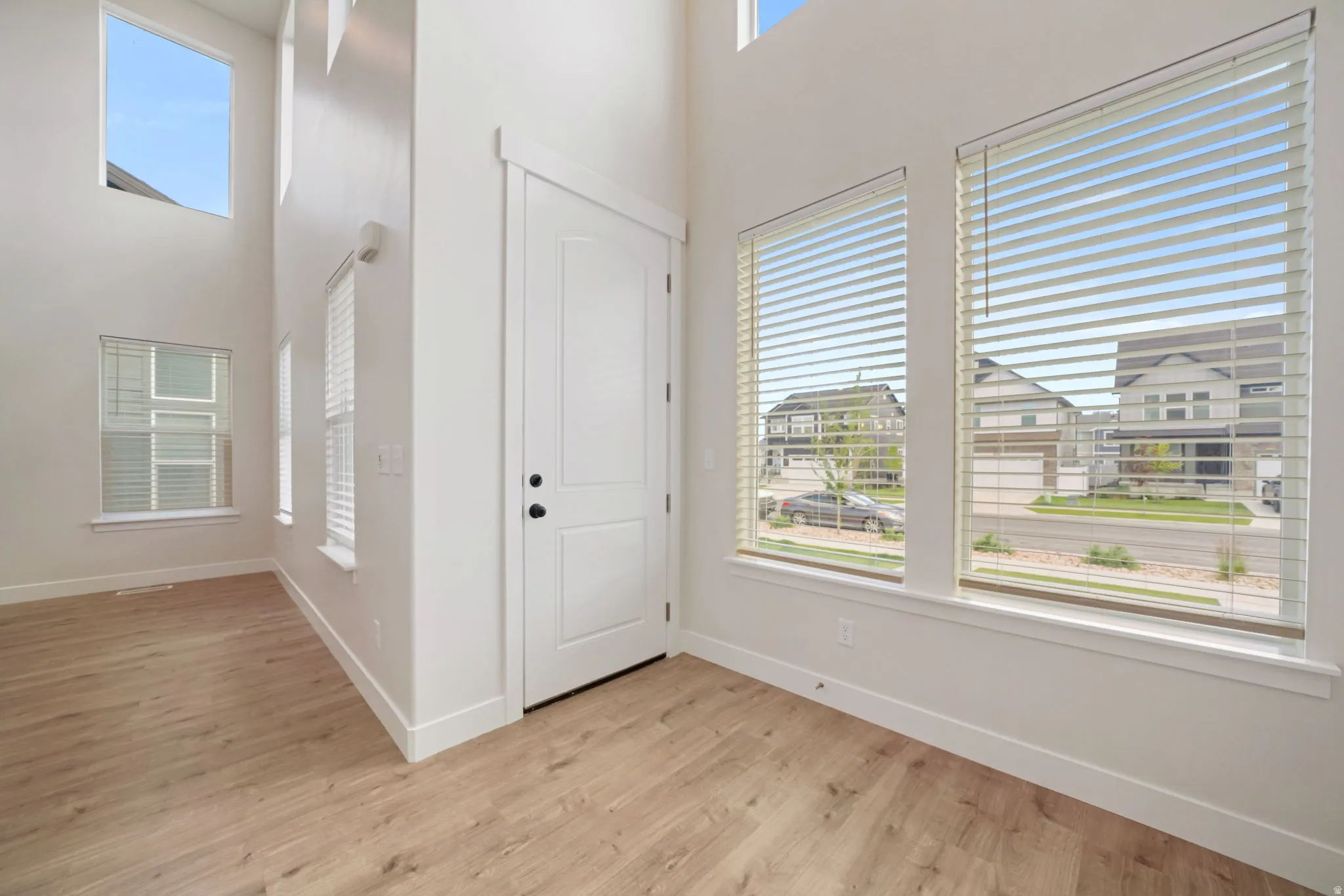 Two-story entry foyer featuring wood-finish flooring, crisp white walls, and multiple windows with blinds