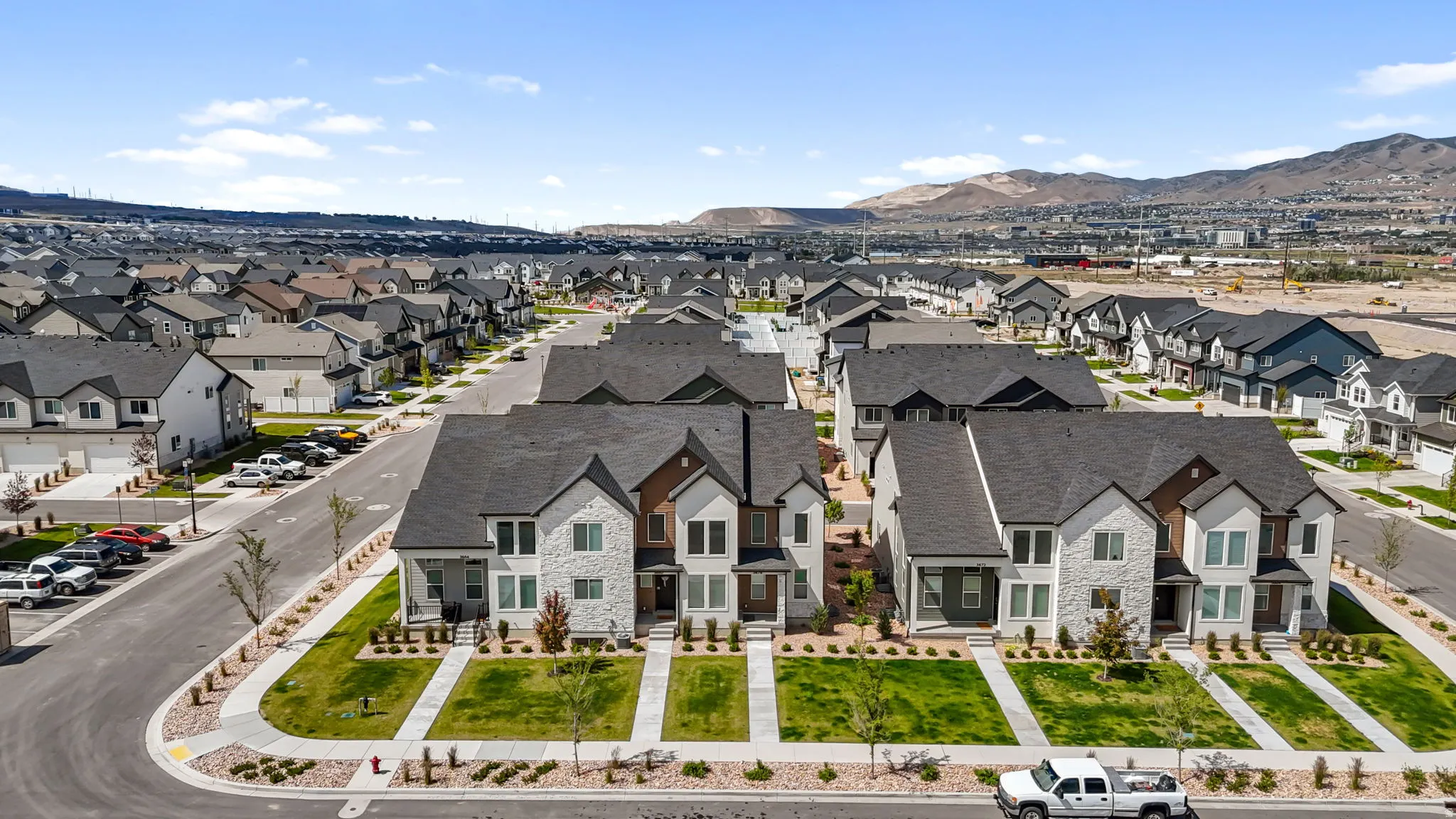 Contemporary residential development featuring a collection of two-story homes with dark shingle roofs, light-toned stone and siding exteriors, and well-maintained front lawns