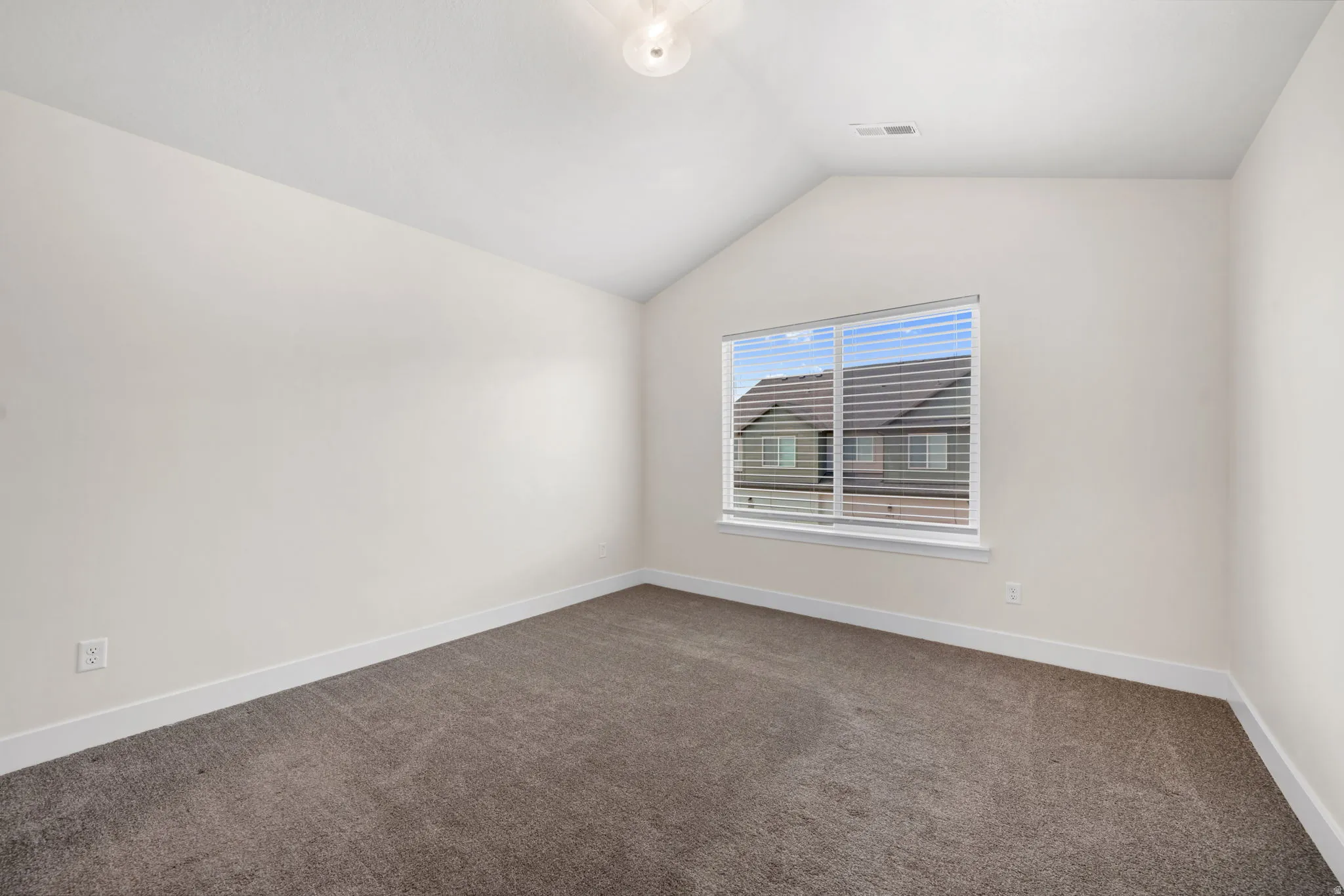 Carpeted room featuring a vaulted ceiling and a window with blinds
